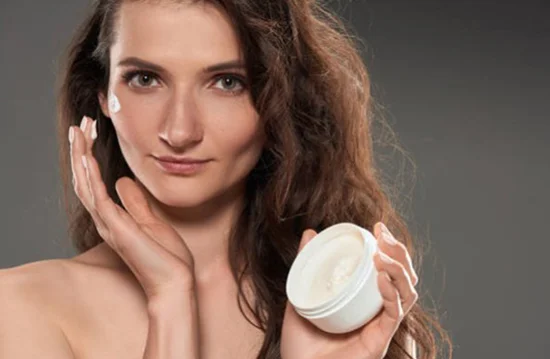 Close up of a pretty woman both applying and displaying a jar of organic face cream